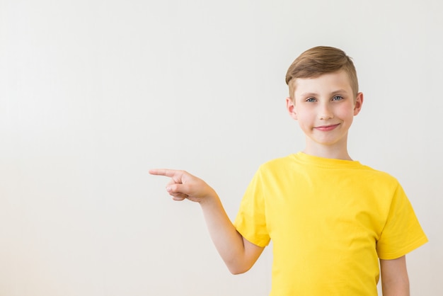 Il giovane ragazzo teenager sorridente mostra il suo dito a lato