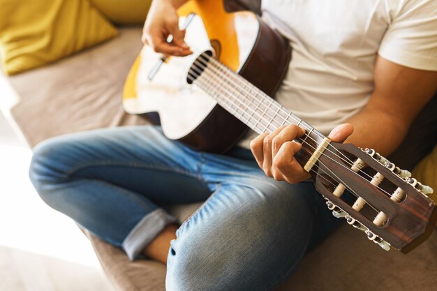 Il giovane seduto sul divano suona casualmente la chitarra acustica in una stanza illuminata