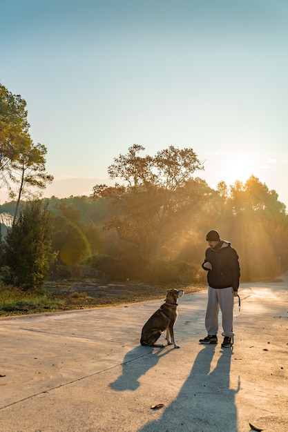 Il giovane si diverte con il suo cane in natura con i raggi del sole mattutino ama il mio cane