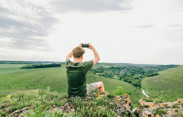 Il giovane si siede su una roccia di montagna e scatta una foto del paesaggio ucraino Viaggio in Ucraina