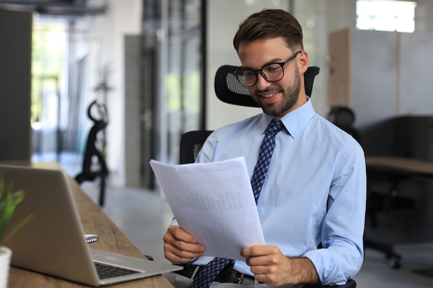 Il giovane sta lavorando con i documenti mentre è seduto in ufficio. Imprenditore di successo sta studiando documenti con sguardo attento e concentrato.