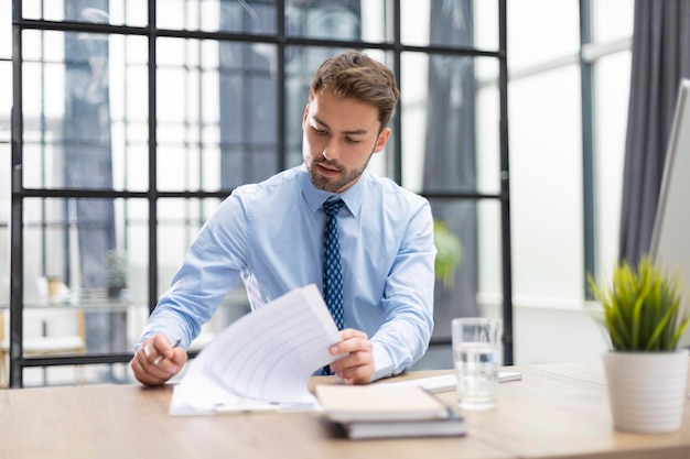 Il giovane sta lavorando con le carte mentre è seduto in ufficio L'imprenditore di successo sta studiando i documenti con uno sguardo attento e concentrato