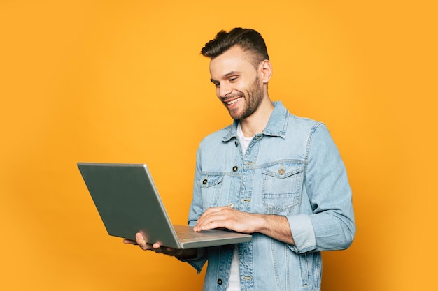 Il giovane studente moderno o l'uomo d'affari sta lavorando con il computer portatile in mano su sfondo giallo