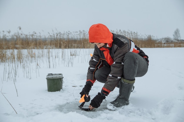 Il giovane su un pescatore di inverno del lago nevoso mette l'esca