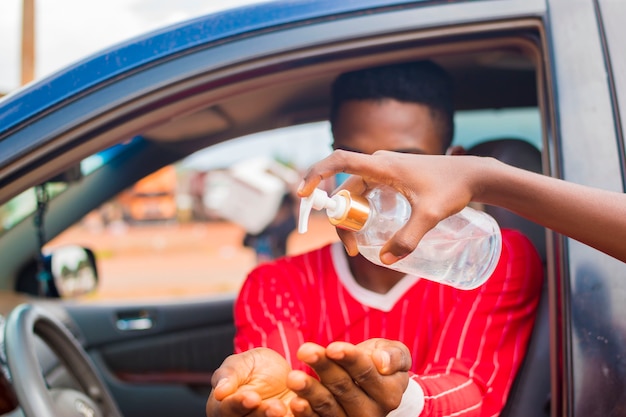 Il giovane tassista africano che indossa la maschera per il viso previene, previene, si impedisce di scoppiare nella società e usa il disinfettante per le mani per lavarsi le mani