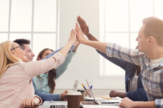 Il giovane team aziendale allegro sta dando il cinque al gruppo, celebrando il progetto di successo, la cooperazione e il concetto di teambuilding, copia spazio