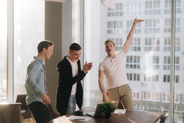 Il giovane team felice di affari sta celebrando la conclusione positiva di un affare importante e si stringe la mano l'un l'altro. Concetto di lavoro di squadra giovani startupper.