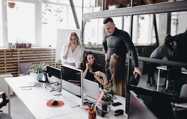 Il giovane team lavora alle scrivanie con un computer e laptop in un ufficio open space moderno e leggero