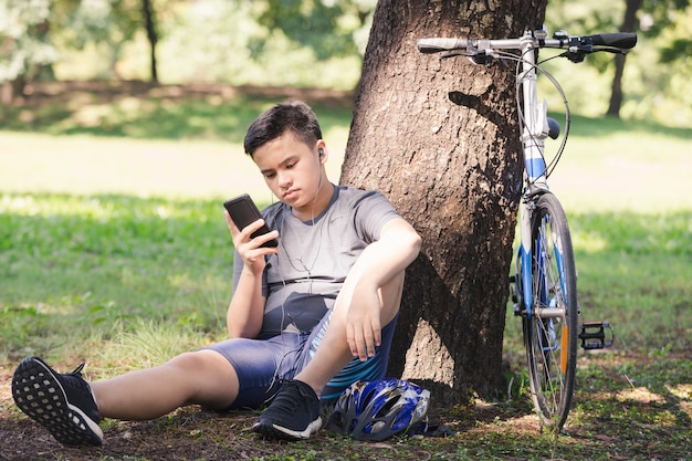 Il giovane telefono del gioco del ragazzo si distende la bicicletta