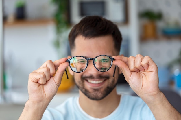 Il giovane tiene gli occhiali con lenti diottriche e guarda attraverso di loro il problema della correzione della vista della miopia