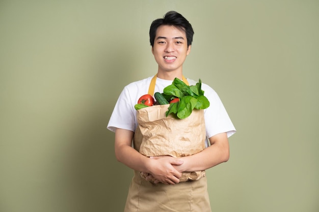 Il giovane tiene in mano una borsa piena di verdure su sfondo bianco