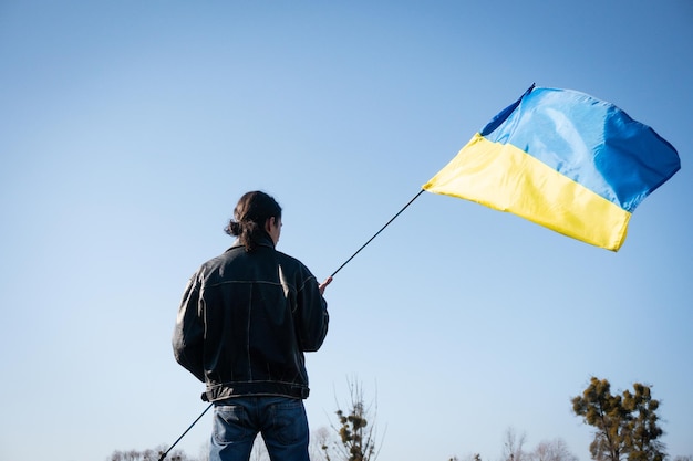 Il giovane tiene la bandiera dell'ucraina nel patriota del campo