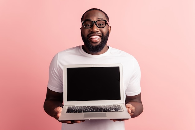 Il giovane uomo africano sorridente che sta e che usa il computer portatile mostra lo spazio vuoto del desktop