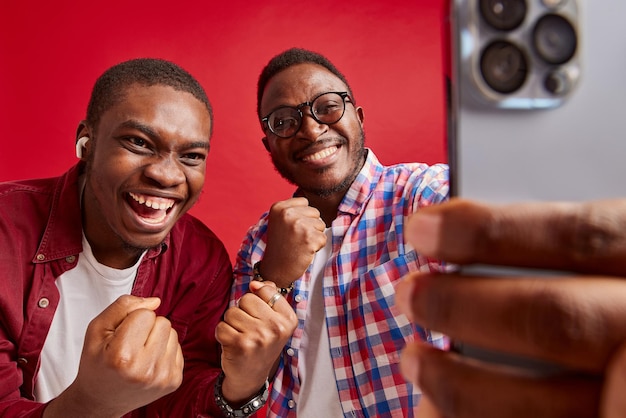Il giovane uomo afroamericano si rallegra con le mani alla macchina fotografica isolata sul ritratto in studio di sfondo rosso