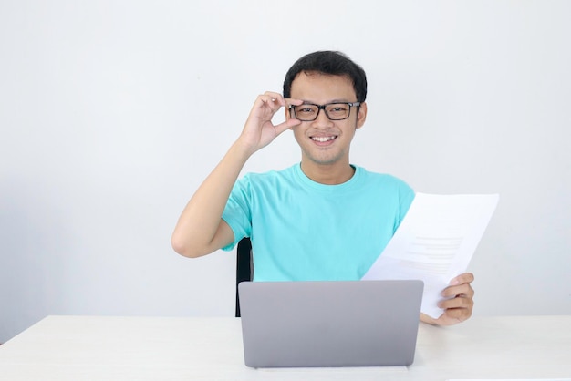 Il giovane uomo asiatico è sorridente e felice quando lavora su un laptop e documenta un uomo indonesiano che indossa una camicia blu