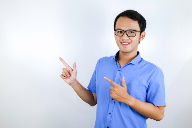 Il giovane uomo asiatico indossa una camicia blu è felice e sorridente quando indica e guarda nell'orologio isolato su sfondo bianco