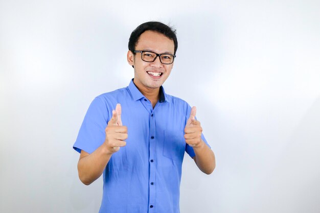 Il giovane uomo asiatico indossa una camicia blu e occhiali con la faccia sorridente felice e i pollici in su