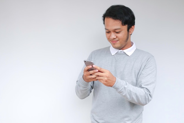 Il giovane uomo asiatico intelligente è felice e sorridente quando utilizza lo smartphone in background