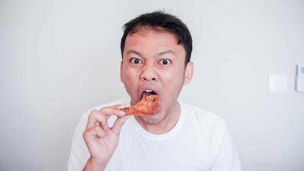 Il giovane uomo asiatico sta mangiando la camicia bianca di usura del pollo fritto