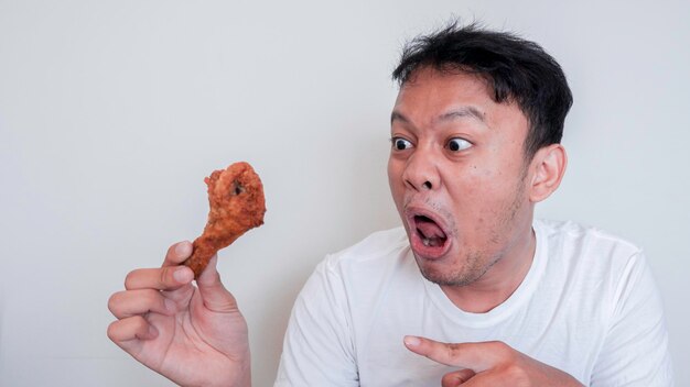 Il giovane uomo asiatico sta mangiando pollo fritto indossa una camicia bianca sentendosi arrabbiato e pazzo