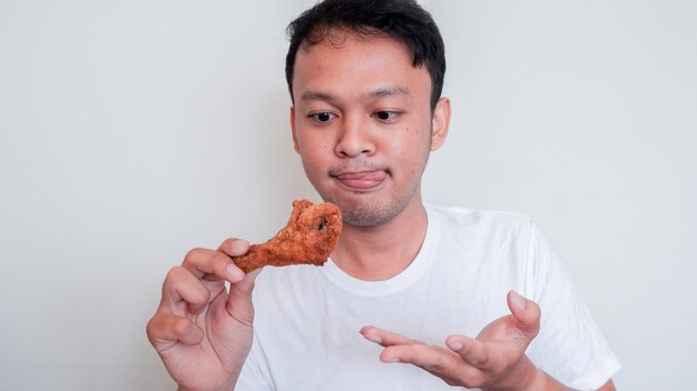 Il giovane uomo asiatico sta mangiando pollo fritto indossa una camicia bianca sentendosi tentato e affamato