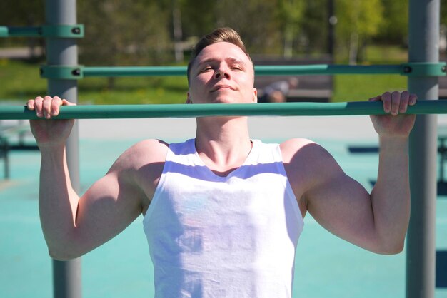 Il giovane uomo atletico sportivo si sta allenando all'aperto durante la giornata di sole estiva facendo pull up