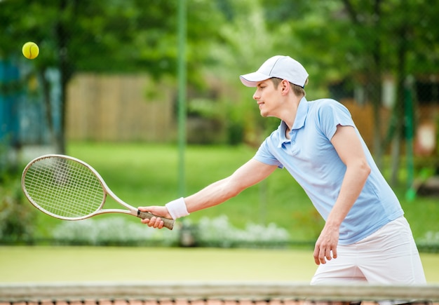 Il giovane uomo attraente gioca a tennis alla corte di mattina.