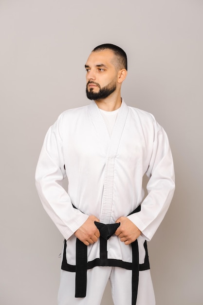 Il giovane uomo barbuto che indossa l'uniforme del taekwondo tiene la cintura nera