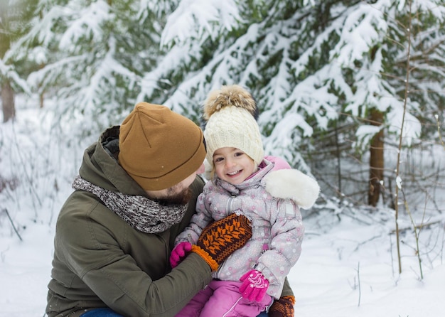 Il giovane uomo barbuto con la bambina si diverte nella foresta innevata in inverno