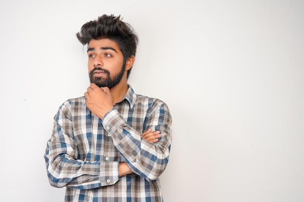 Il giovane uomo barbuto ispanico che indossa una camicia a quadri su sfondo bianco con un'espressione positiva ha un ampio sorriso interessato Guarda lì per favorecercando qualcosa o trovato qualcosa