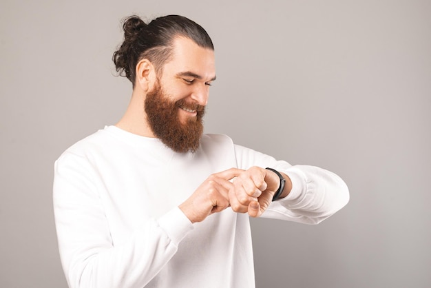 Il giovane uomo barbuto moderno controlla il suo orologio intelligente da polso mentre sorride