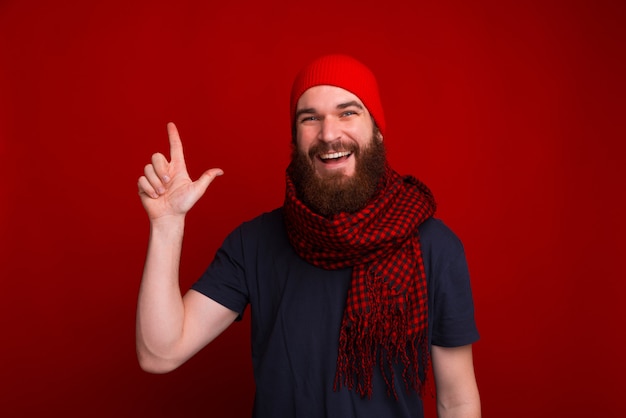 Il giovane uomo barbuto sorridente sta indicando su allo spazio della copia e sta esaminando la macchina fotografica.