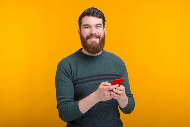 Il giovane uomo barbuto sta scrivendo qualcosa sul suo telefono o sta navigando in Internet.