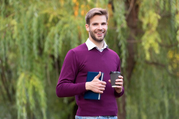 Il giovane uomo bello allegro beve il caffè del mattino all'aperto