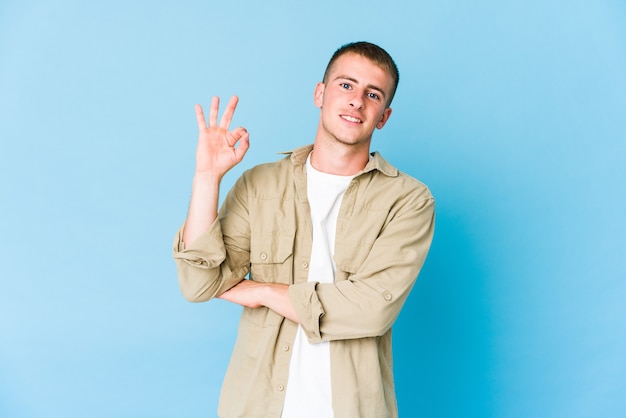 Il giovane uomo bello caucasico strizza l'occhio e tiene un gesto giusto con la mano.