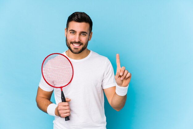 Il giovane uomo bello che gioca il volano ha isolato la mostra del numero uno con il dito