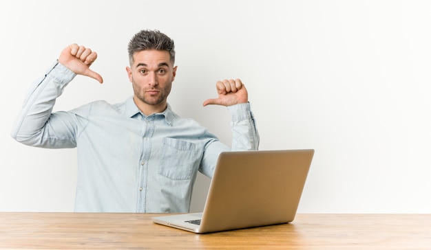 Il giovane uomo bello che lavora con il suo laptop si sente orgoglioso e sicuro di sé, esempio da seguire.