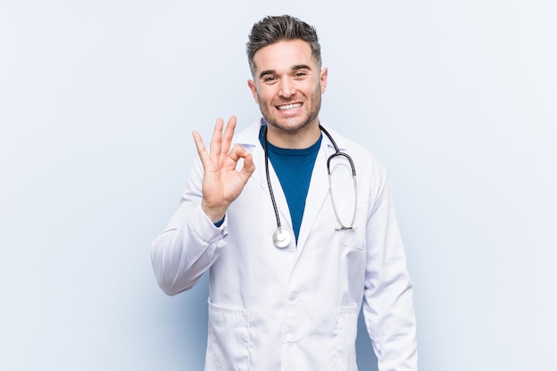 Il giovane uomo bello del medico sbatte le palpebre un occhio e tiene un gesto giusto con la mano.