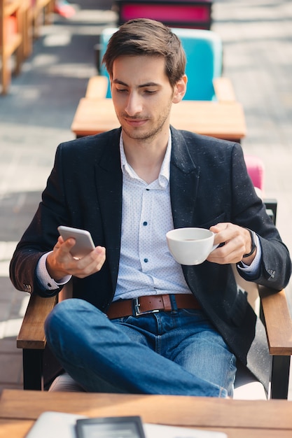 Il giovane uomo bello gode del caffè mentre manda un sms