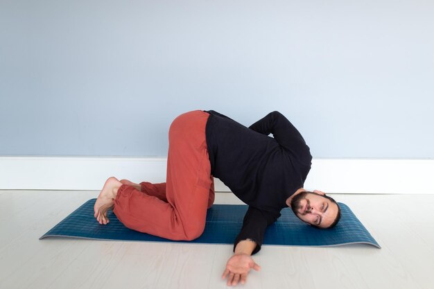 Il giovane uomo bianco dai capelli lunghi caucasico sta eseguendo yoga in uno studio o in una casa