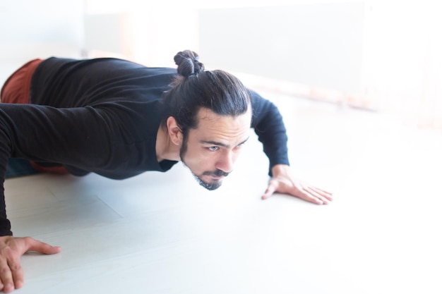 Il giovane uomo bianco dai capelli lunghi caucasico sta eseguendo yoga in uno studio o in una casa