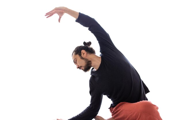 Il giovane uomo bianco dai capelli lunghi caucasico sta eseguendo yoga in uno studio o in una casa