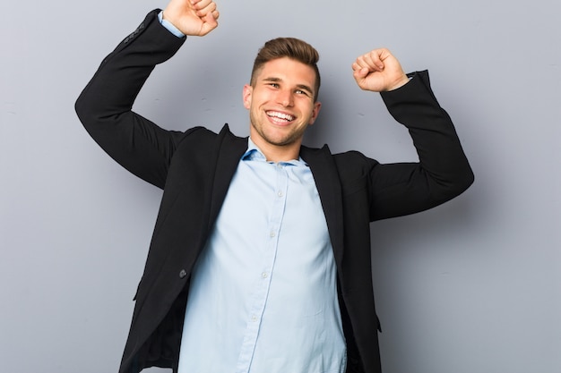 Il giovane uomo caucasico bello che celebra un giorno speciale, salta e alza le braccia con energia.