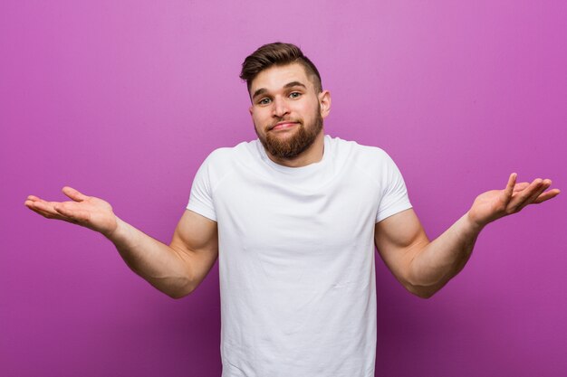 Il giovane uomo caucasico bello che dubita e che lo scrolla le spalle mette in discussione il gesto.