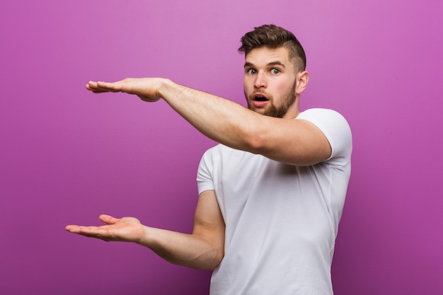 Il giovane uomo caucasico bello ha colpito e stupito tenendo uno spazio della copia fra le mani.