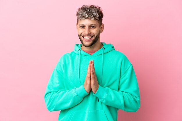 Il giovane uomo caucasico bello isolato su sfondo rosa tiene insieme il palmo. La persona chiede qualcosa