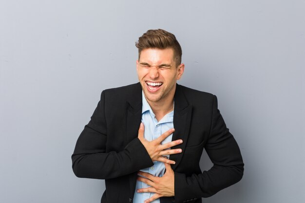 Il giovane uomo caucasico bello ride felicemente e si diverte a tenere le mani sullo stomaco.