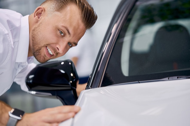 Il giovane uomo caucasico bello sta controllando la superficie dell'auto