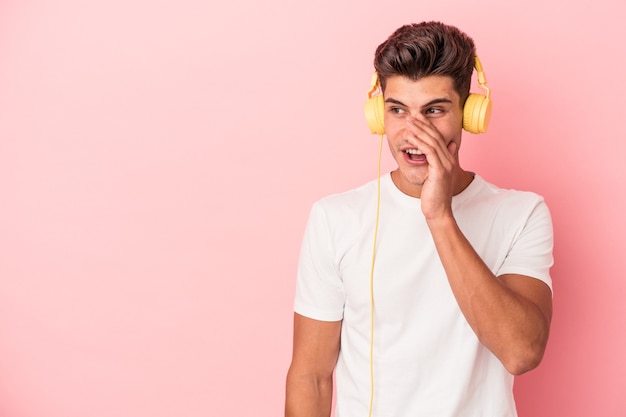 Il giovane uomo caucasico che ascolta musica isolata su sfondo rosa sta dicendo una notizia segreta di frenata calda e sta guardando da parte