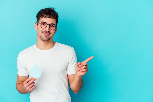 Il giovane uomo caucasico che celebra la giornata mondiale dell'acqua ha isolato sorridendo e indicando da parte, mostrando qualcosa in uno spazio vuoto.